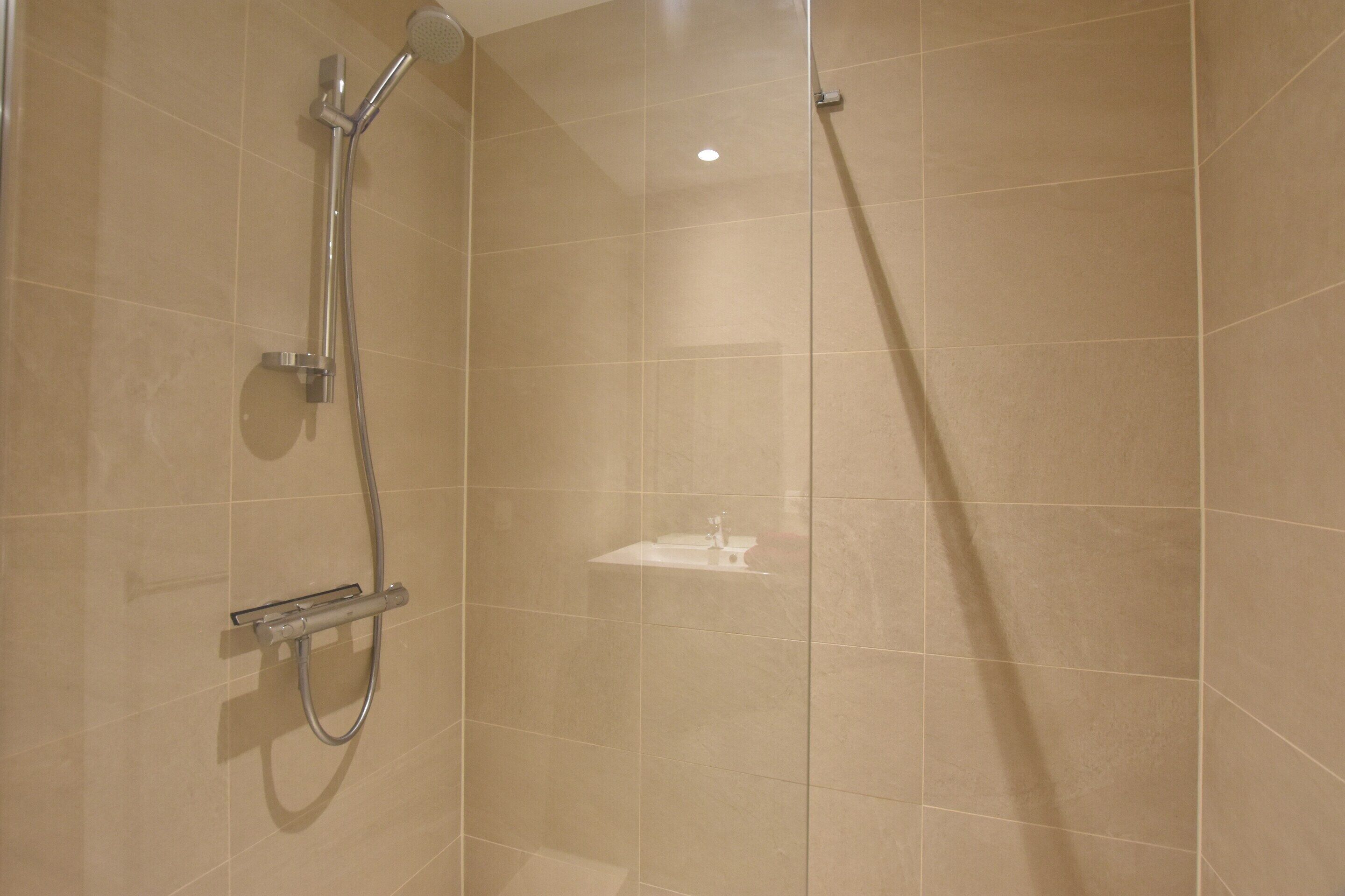 Une douche équipée d’un pommeau de douche à main et d’un robinet mural.