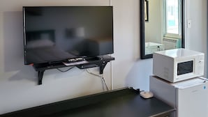 Un televisor de pantalla plana montado en la pared, un microondas sobre una mesita y un aparador con cajones.