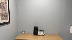 Una oficina pequeña y privada con un escritorio de madera, una silla blanca y una estación de café.