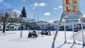 Letrero de motel con los mensajes 'VACANCY' y 'WELCOME', rodeado por un estacionamiento cubierto de nieve y un edificio con múltiples ventanas.