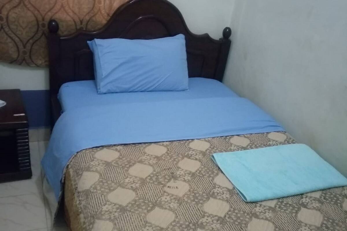 A single bed with a patterned bedspread and a blue pillow.