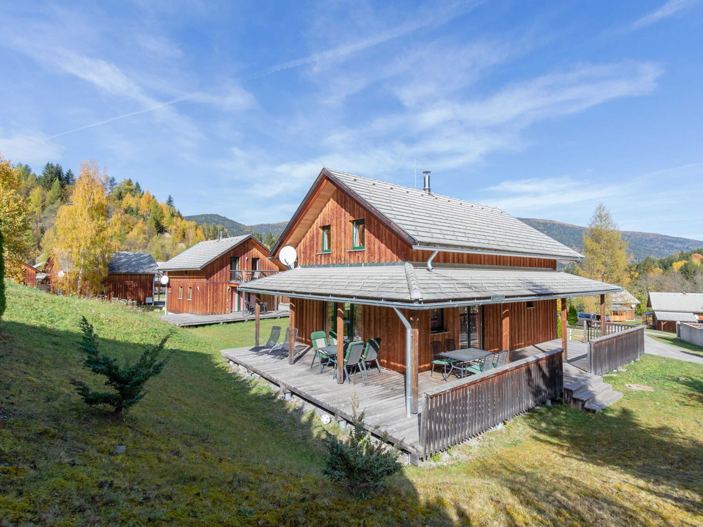 A wooden cabin with a covered patio, surrounded by a grassy area and trees.