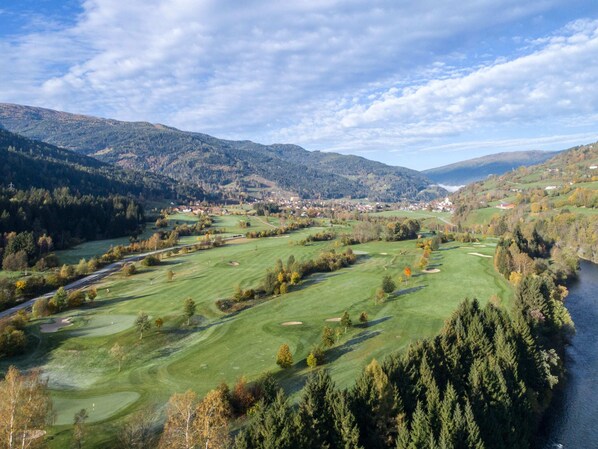 A golf course with a river, forested hills, and a small town in the background.