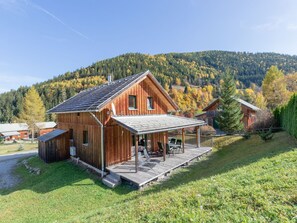 A wooden cabin with a porch and a covered patio, surrounded by a forested hillside.