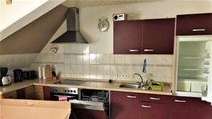 Une cuisine équipée d’une cuisinière, d’un four, d’un lave-vaisselle et d’un four à micro-ondes. On y trouve un évier avec un robinet, ainsi que des placards au-dessus du plan de travail.