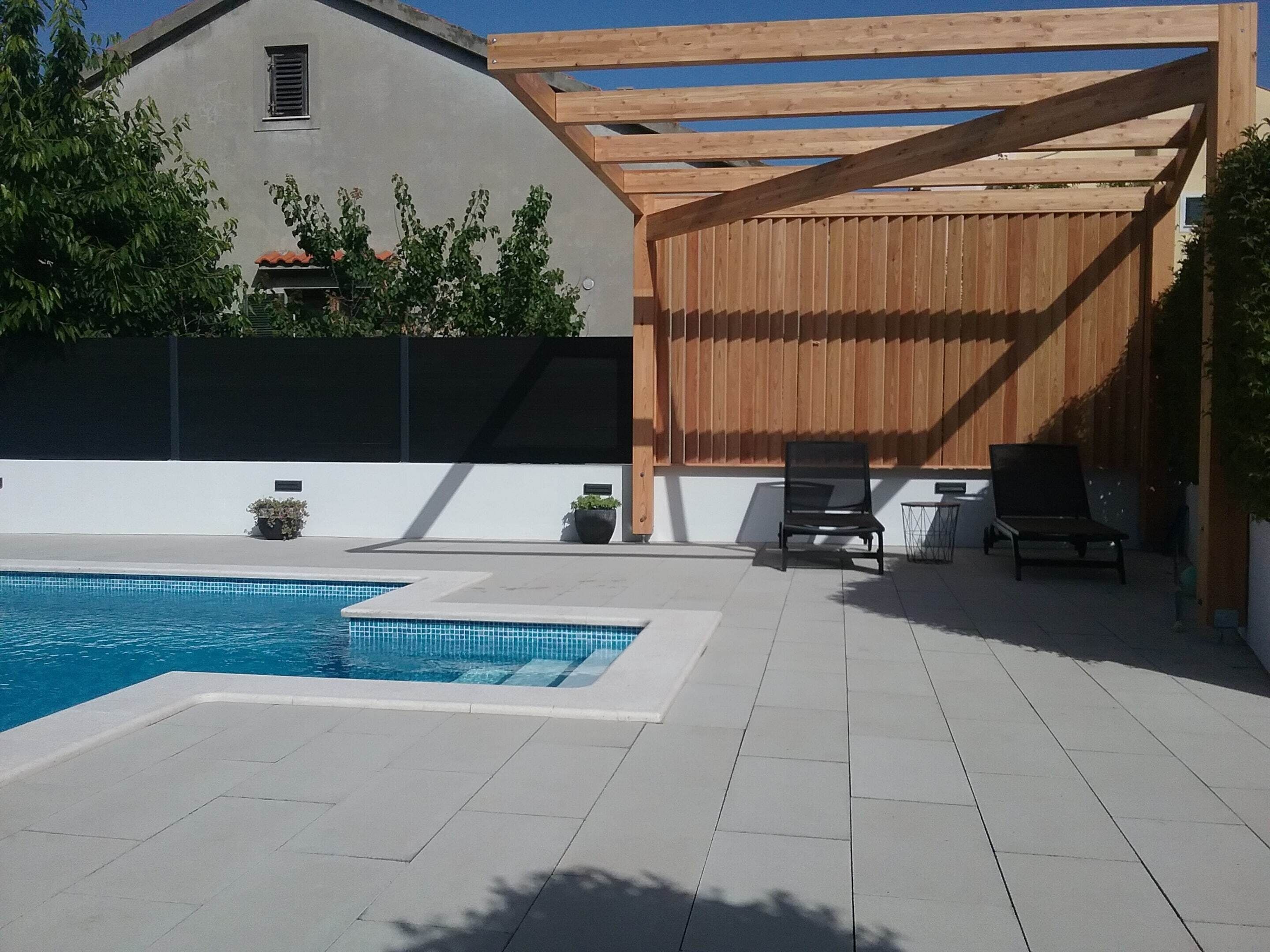 A swimming pool with a wooden pergola and lounge chairs.