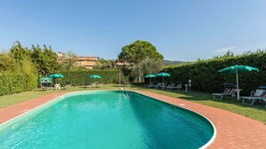 A rectangular swimming pool with a brick border, surrounded by green umbrellas and lounge chairs.