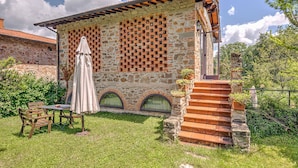 Un bâtiment en pierre avec un toit en tuiles, une terrasse avec une table et des chaises, et un escalier menant à l’entrée.