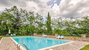 Une piscine rectangulaire bordée d’une terrasse en pierre, entourée de verdure et d’un mur de pierre.
