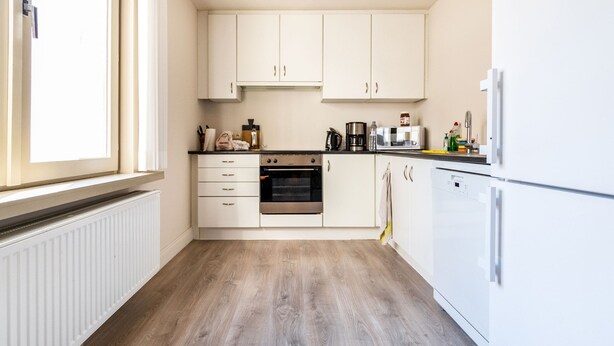 Una cocina moderna con armarios blancos, horno empotrado y refrigerador.