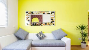 A modern living room with a white sectional sofa, a yellow accent wall, and a decorative wall art piece. - Simplistic Apartment in Vir With Garden (Vir)