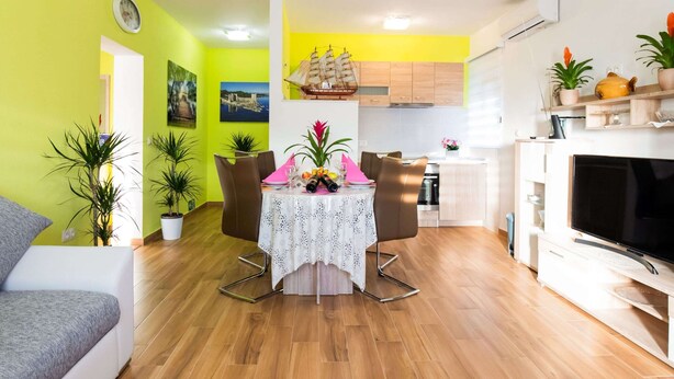 A modern living room with a dining area, wooden flooring, and a kitchen in the background. - Simplistic Apartment in Vir With Garden (Vir)