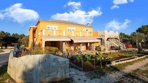 A two-story building with a yellow facade, a balcony, and a staircase leading to an upper level. - Simplistic Apartment in Vir With Garden (Vir)