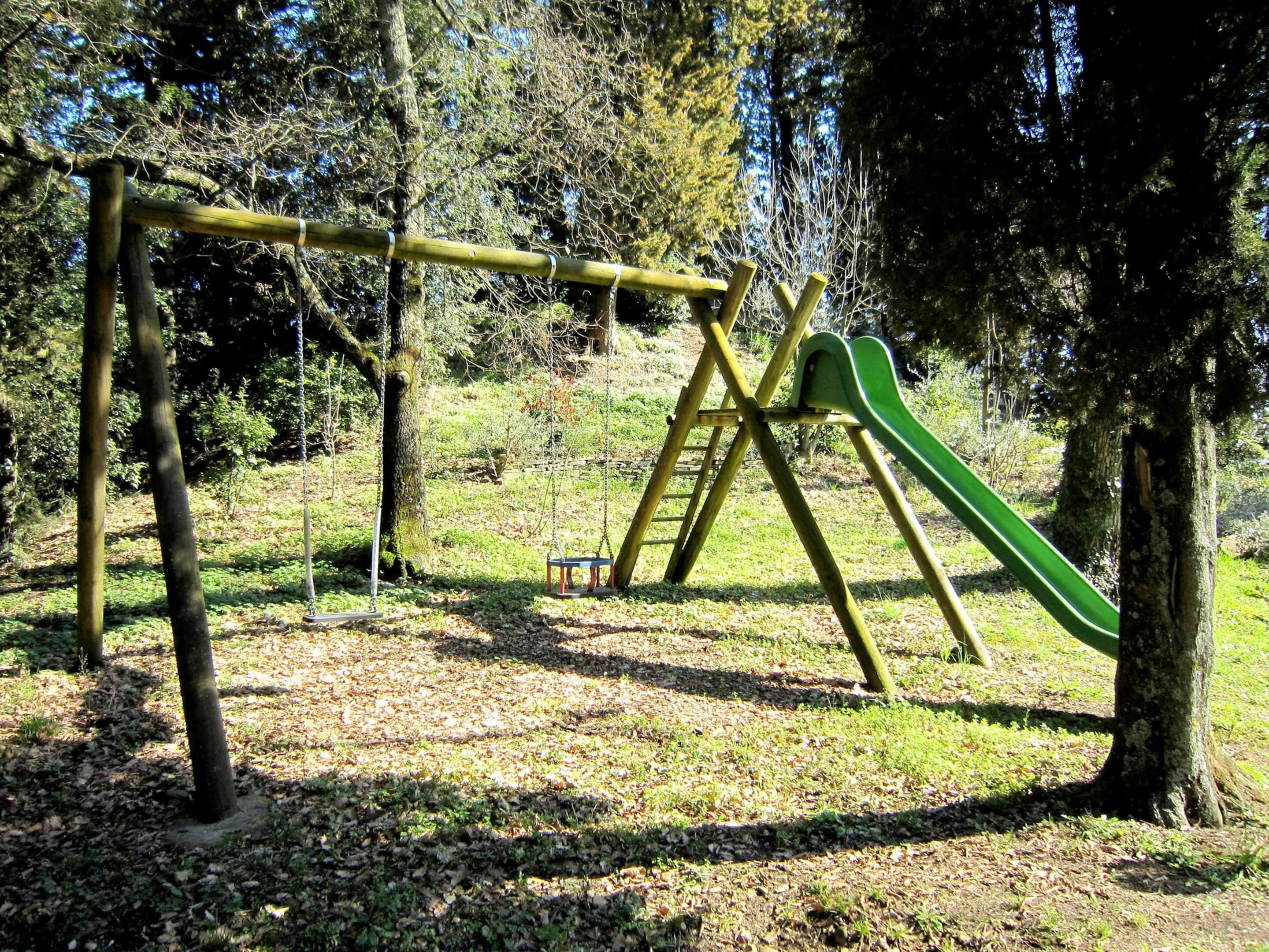 A playground with a swing set and a slide, surrounded by trees and grass.
