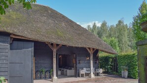 A rustic wooden building with a thatched roof, a covered patio with seating, and a brick pathway. - Posh Holiday Home in Alphen with Hot Tub (Alphen)