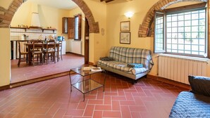 A living room with a checkered sofa, a glass coffee table, and a dining area with wooden chairs and a table. - Belvilla by OYO Loggia (San Casciano in Val di Pesa)