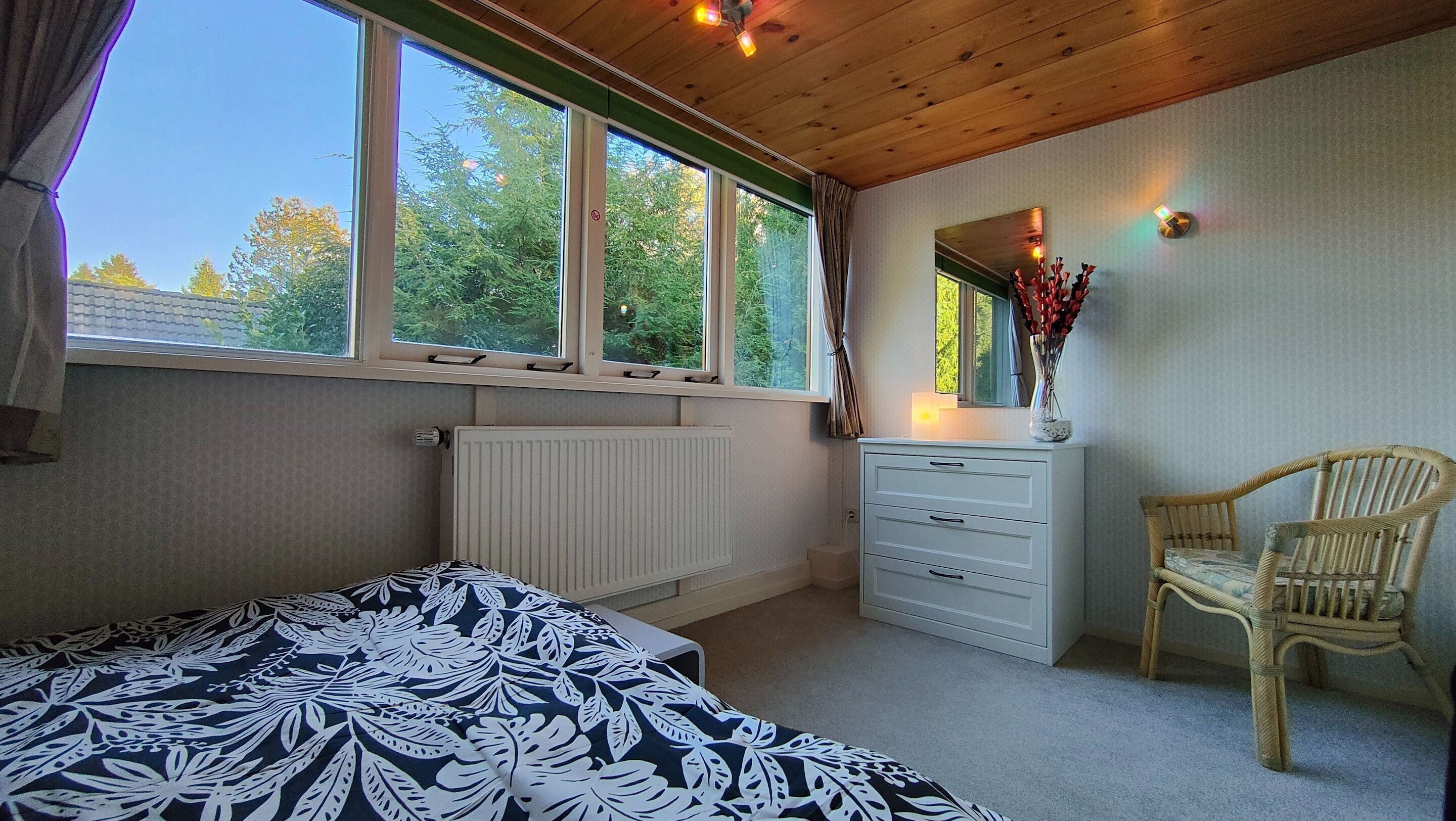 A bedroom with a bed, dresser, chair, and large windows.