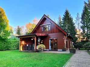 A two-story wooden house with a covered porch, large windows, and a brick pathway leading to the entrance. - Terrace Apartment With Lush Garden (Epe)