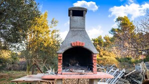 An outdoor brick oven with a chimney, surrounded by trees and a table with cooking utensils. - Delightful Apartment in Vir With Garden (Vir)