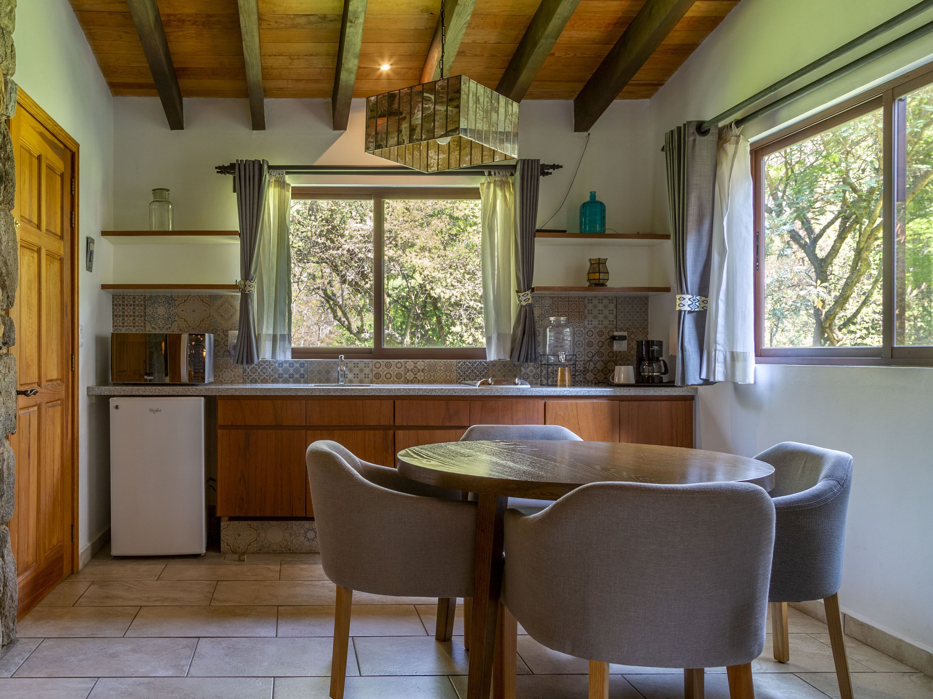 A kitchen with a wooden island, a dining table with four chairs, a refrigerator, and a window with curtains.