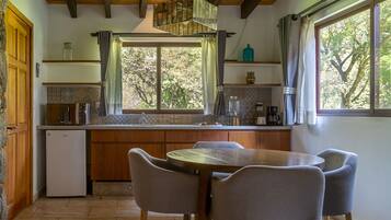 A kitchen with a wooden island, a dining table with four chairs, a refrigerator, and a window with curtains.