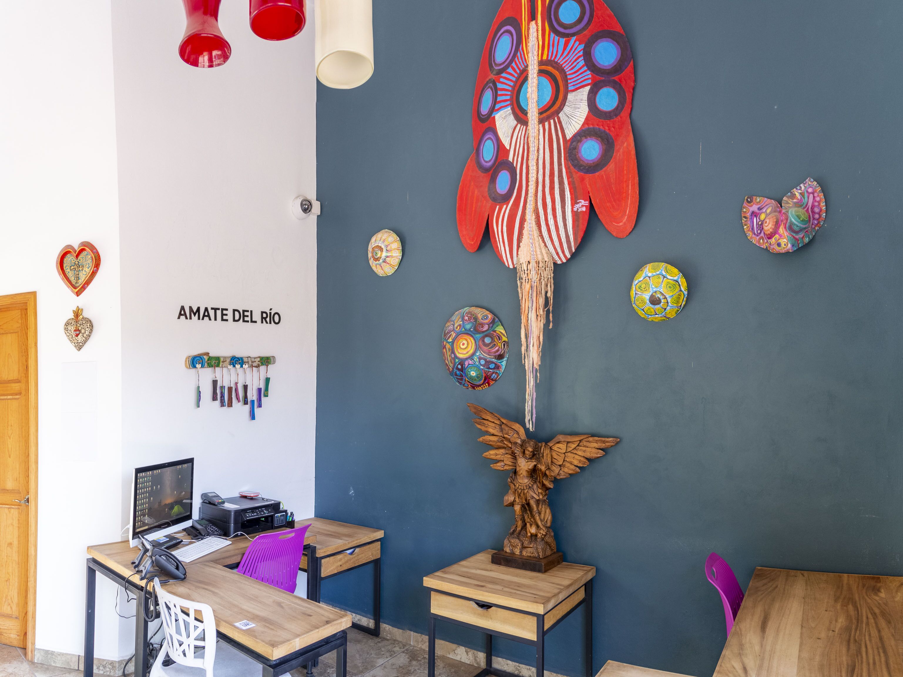 Una habitación con un escritorio de madera, una computadora y una pared decorada con coloridas obras de arte y una gran escultura colgante.