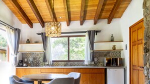 A kitchen with wooden cabinets, a dining table with chairs, a refrigerator, and a window with curtains. - Hotel Amate del Rio (Malinalco)