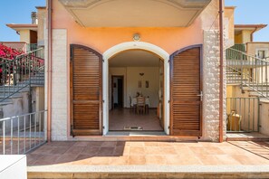 Ein Gebäudeeingang mit überdachter Terrasse, einer Treppe und Blick ins Innere.