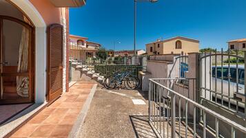 Un quartier résidentiel avec un balcon, un vélo et une voiture garée au loin.