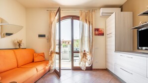 Una habitación con sofá, televisión, zona de cocina y puerta que da a un espacio exterior.