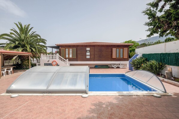 A swimming pool with a cover, a wooden house, and a white fence. - Charming "Casa Rural" with Sea View, Mountain View, Wi-Fi, Garden, Terrace & Pool (Arafo)