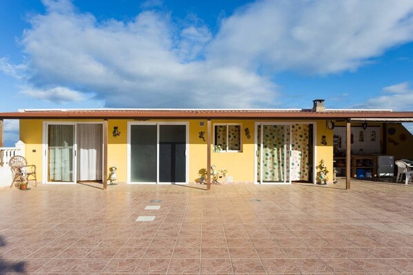 A two-story building with a tiled patio, sliding glass doors, and a small outdoor kitchen area. - Charming "Casa Rural" with Sea View, Mountain View, Wi-Fi, Garden, Terrace & Pool (Arafo)