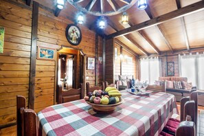 A wooden cabin interior with a dining table, chairs, a fruit bowl, and a cozy seating area.