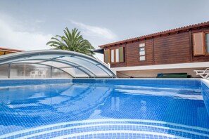 A swimming pool with a glass enclosure, a wooden building with windows, and a palm tree in the background. - Charming "Casa Rural" with Sea View, Mountain View, Wi-Fi, Garden, Terrace & Pool (Arafo)