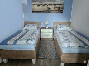 A room with two beds, a small nightstand with a lamp, and a framed picture on the wall.