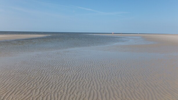 Une plage avec des motifs dessinés dans le sable et un ciel dégagé.