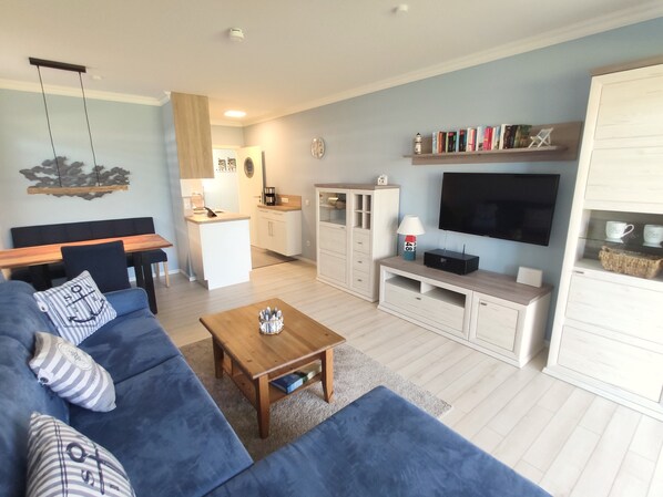 A modern living room with a sofa, coffee table, TV, and kitchen area.