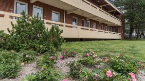 Un immeuble à plusieurs étages, doté d’un toit plat, de balcons et d’un jardin où poussent des fleurs roses.