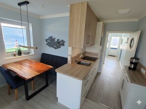 A modern kitchen with a wooden dining table, a built-in sink, and a view of the sea through a window.