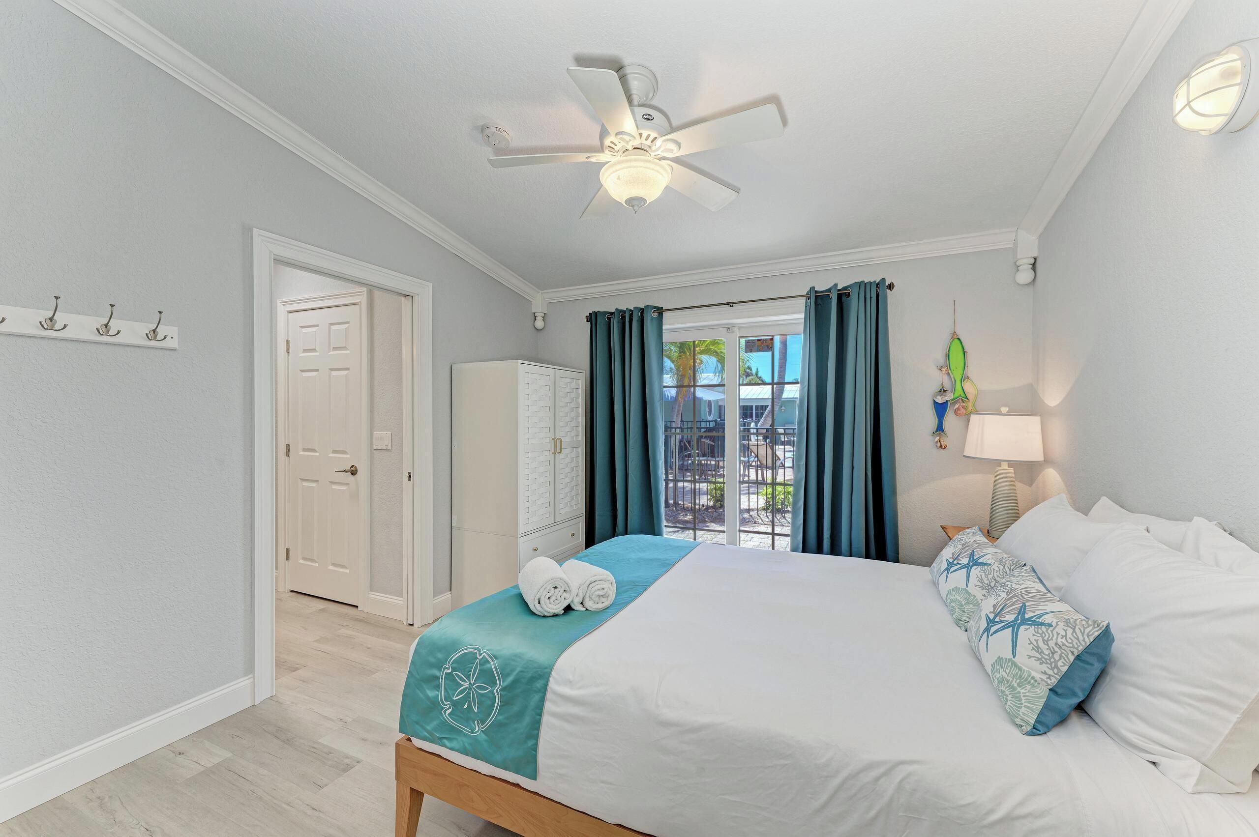 Une chambre d’hôtel avec un lit, un ventilateur de plafond, une fenêtre avec des rideaux et une vue sur l’extérieur.