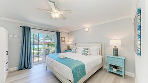 Une chambre à coucher avec un lit, une table de chevet, un ventilateur de plafond et une fenêtre avec des rideaux.