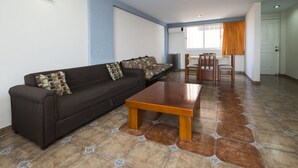 Uma sala de estar com sofá, mesa de centro de madeira, ladrilhos estampados e um espaço de jantar com cadeiras e mesa.