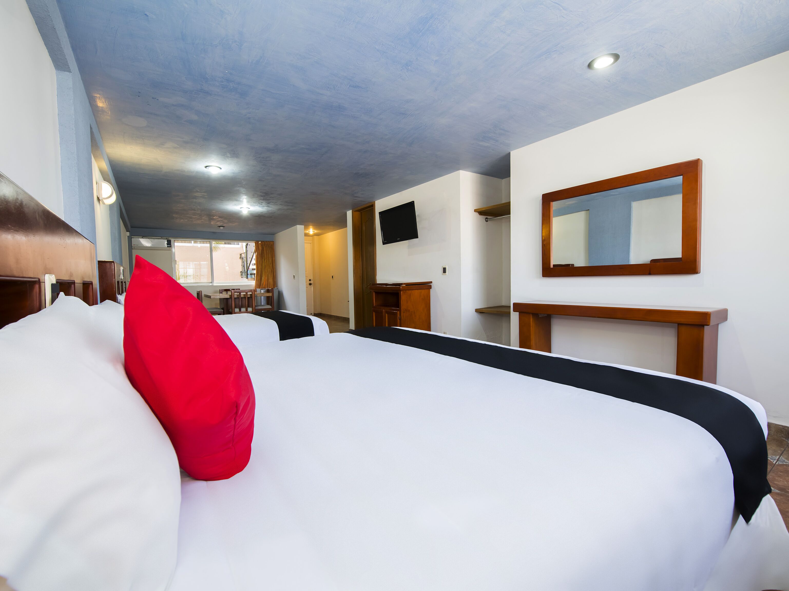 A hotel room with two beds, a TV, a mirror, and a desk.
