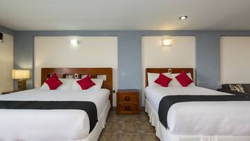 Une chambre d’hôtel avec deux lits, chacun doté de draps blancs et d’oreillers rouges, une table de chevet avec une lampe et un petit tiroir.
