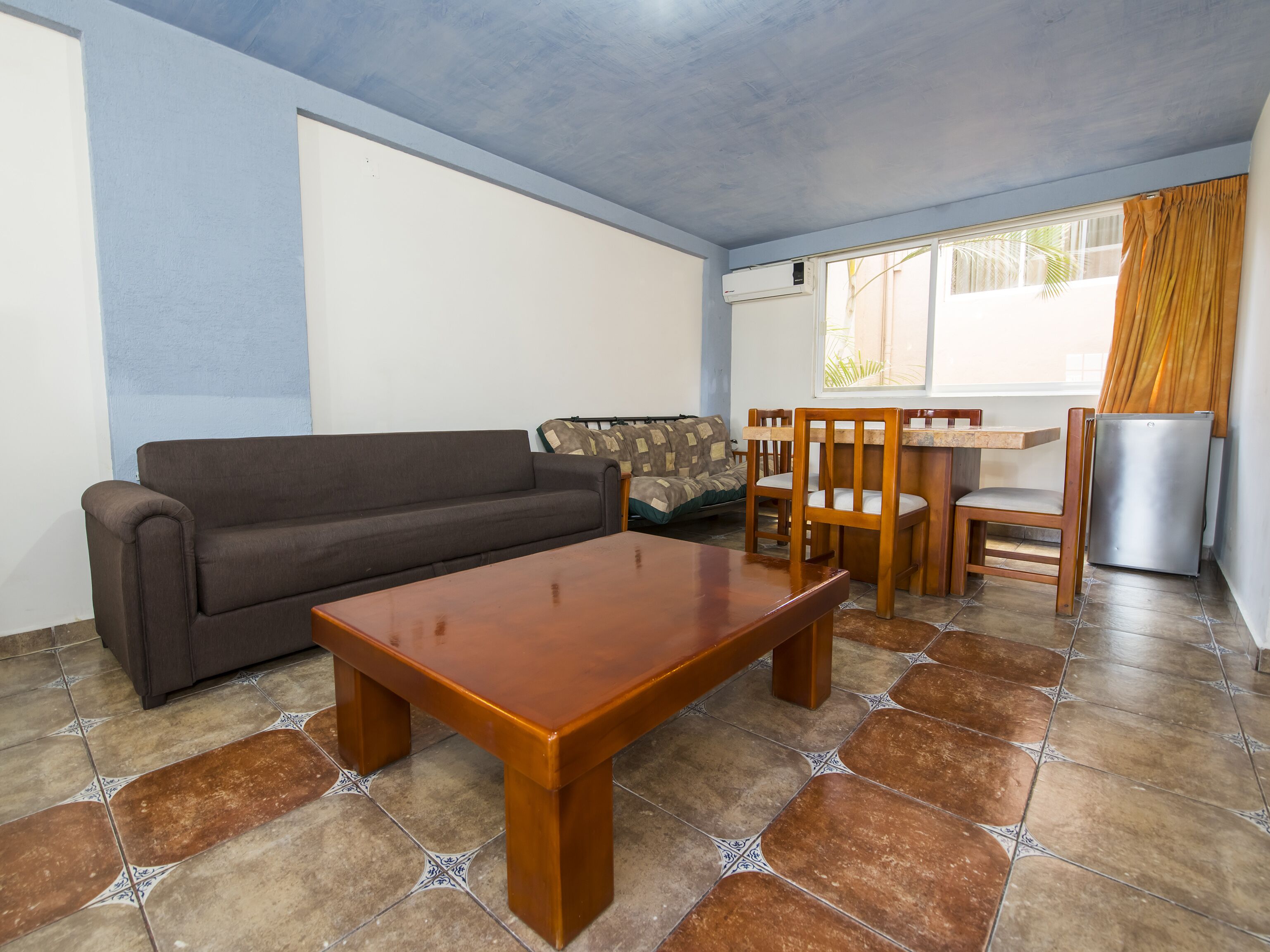 Un salon comprenant un canapé, une table à manger en bois, des chaises et un réfrigérateur.