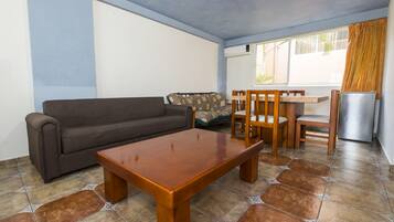Un salon comprenant un canapé, une table à manger en bois, des chaises et un réfrigérateur.