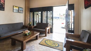 Uma sala de estar ampla com sofá, cadeiras e mesa de centro. Há uma porta que dá para o exterior, e o chão é coberto por azulejos.