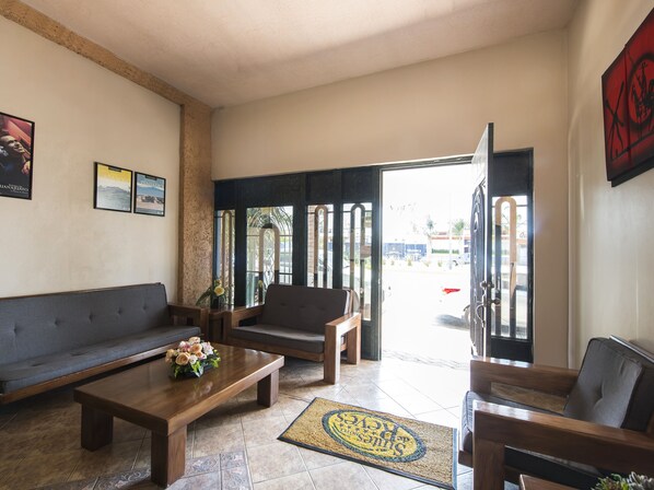 Amplia sala de estar con sofá, sillas y una mesita de centro. Hay una puerta que da al exterior, y el piso está cubierto de baldosas.