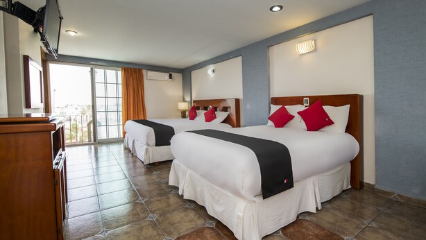Quarto de hotel com duas camas, uma escrivaninha de madeira e uma janela grande com cortinas.