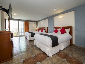 Habitación de hotel con dos camas, un escritorio de madera y un amplio ventanal con cortinas.